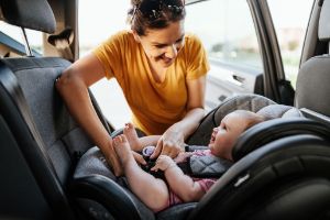 Mutter lächelt ihr Kind im Auto-Kindersitz an.