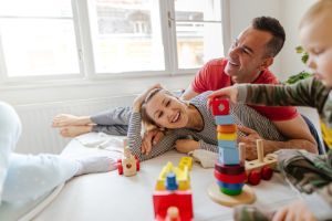 Eltern spielen lachend mit ihren 2 kleinen Kindern auf dem Sofa mit Holzspielzeug.