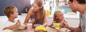 Eltern sitzen mit ihren 2 kleinen Kindern am Küchentisch und frühstücken Müsli.