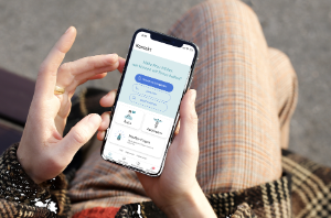 Eine Person sitzt auf einer Bank draußen und tippt mit dem Finger auf dem Smartphone in der Anwendung der Online-Sprechstunde.