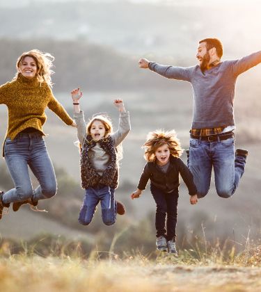 Eine Familie steht auf einer Wiese und springt in die Luft.